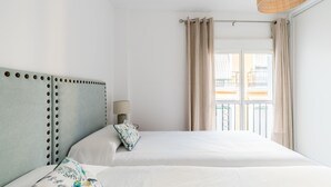 A hotel room with two beds, a headboard with a circular pattern, a window with curtains, and a hanging light fixture. - Terraza Catedral Olehousing 4 (Sevilla)