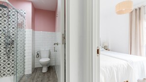 A bathroom with a shower, toilet, and a bed with a white bedspread. - Terraza Catedral Olehousing 4 (Sevilla)