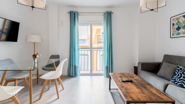 A modern living room with a glass dining table, white chairs, a wooden coffee table, and a grey sofa. - Terraza Catedral Olehousing 4 (Sevilla)