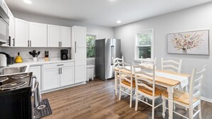 Une cuisine moderne avec des meubles blancs, un réfrigérateur en acier inoxydable et un coin repas comprenant une table en bois et des chaises blanches.