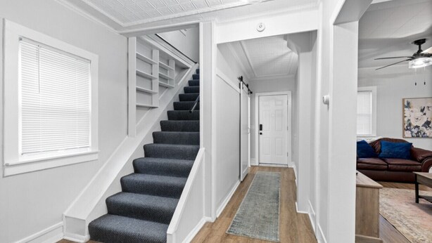 Un escalier menant à un palier avec une porte, un canapé en cuir marron et un ventilateur de plafond dans une pièce aux murs blancs et au plancher en bois.