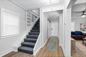A staircase leading to a landing with a door, a brown leather sofa, and a ceiling fan in a room with white walls and wooden flooring. - Village of Fairport - 2 BDRM w/Onsite Parking (Fairport)