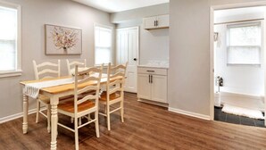 Un coin repas avec une table et des chaises en bois, une cuisine avec des meubles blancs et une salle de bain avec une baignoire.