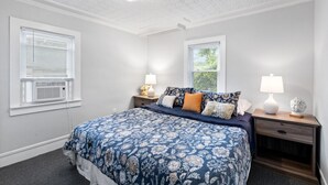 Une chambre à coucher comprenant un lit, deux tables de chevet, une fenêtre et un plafond orné d’un motif décoratif.