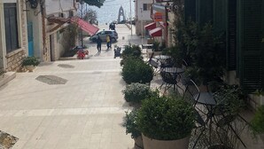 Un vicolo stretto fiancheggiato da edifici, con posti a sedere all'aperto e vista sul mare in lontananza.