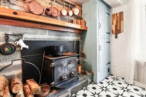 Une cuisine avec un four ancien, des casseroles en cuivre et une étagère en bois.