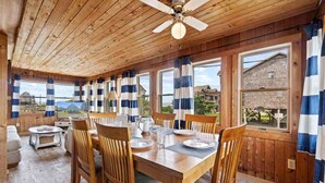 A wooden dining room with a table set for four, large windows with striped curtains, and a ceiling fan. - Canalfront Dog Friendly w/ Hot Tub, Boat Dock, Game Room, Nearby Beach Access (Avon)