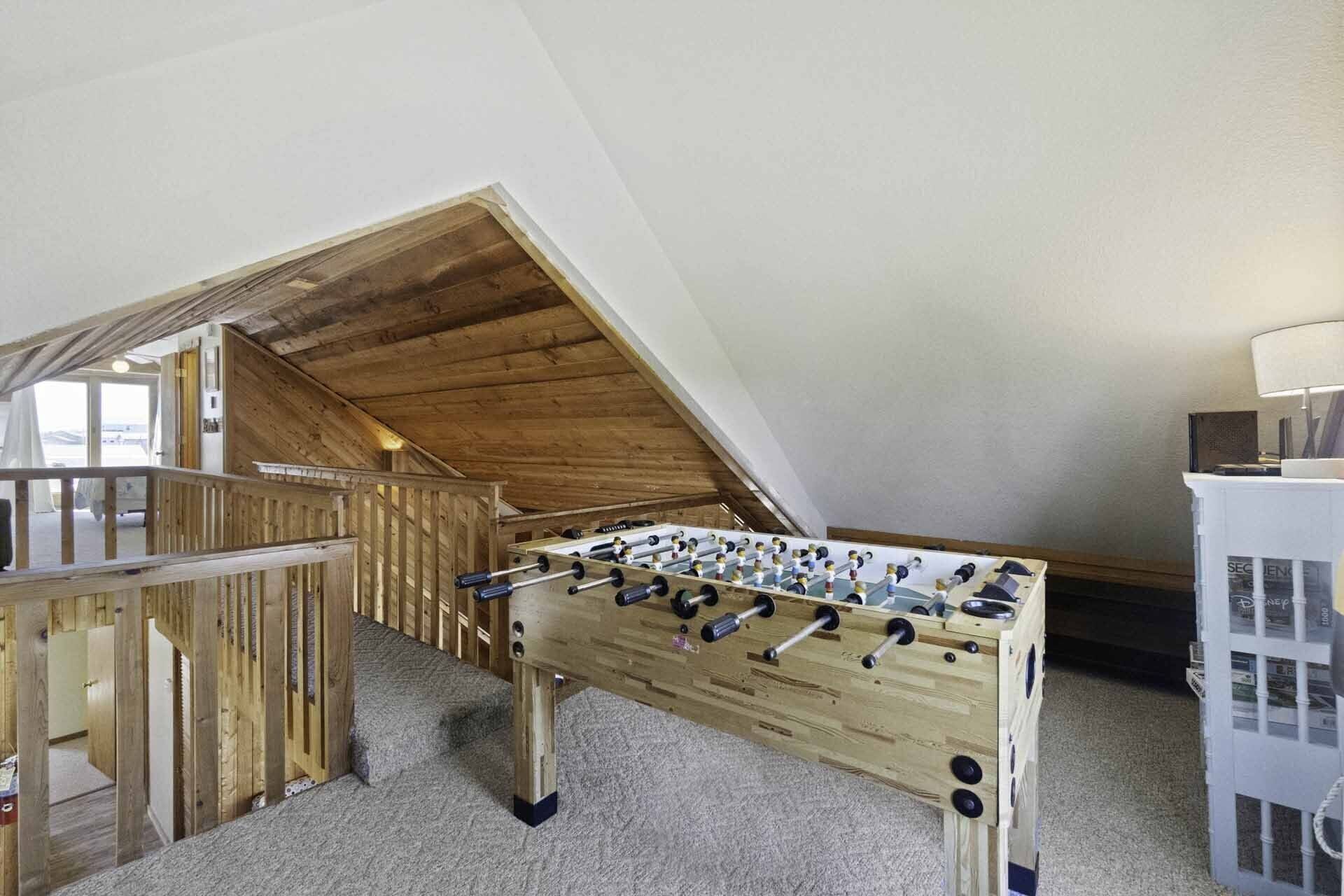 Une table de baby-foot dans une pièce dotée d’un plafond en pente et de poutres en bois.