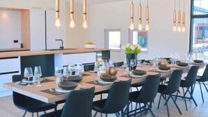A modern dining area with a long table set for six, black chairs, and pendant lighting.