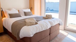 A bedroom with a large bed, a wooden wardrobe, and a view of the sea through a large window.