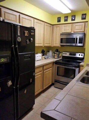Kitchen area with refrigerator, microwave, and stove, featuring wooden cabinets and a tiled backsplash.