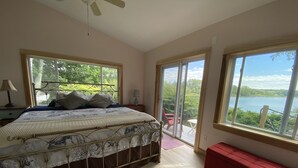 Un dormitorio con una cama, un banco rojo y ventanas amplias que dan a un lago.
