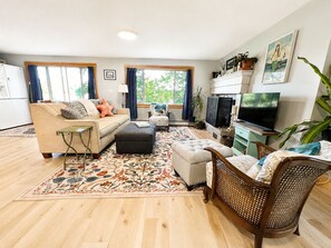 A living room with a sofa, ottoman, TV, and a dining area with a chair.