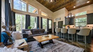 A spacious living room with a large window, a fireplace, and a kitchen area with bar stools.
