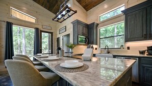 A kitchen with a large island, dark cabinets, and a view of the forest.