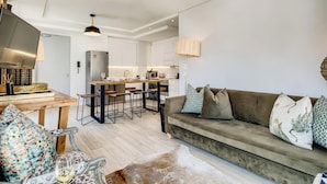 A modern living room with a sofa, a dining area with a table, and a kitchen in the background. - Beautiful Apartment with Mountain Views (404 on N) (Cape Town)