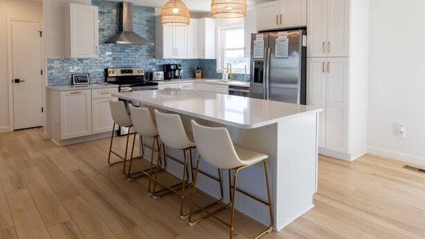A modern kitchen with a large island, white cabinetry, a stainless steel range, and a blue-tiled backsplash.