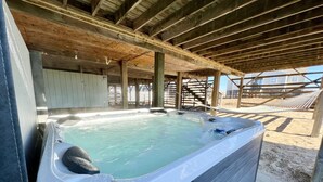 A hot tub under a wooden deck with a sandy ground.