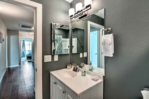 Un baño moderno con un espejo grande, un lavabo blanco y un piso oscuro.