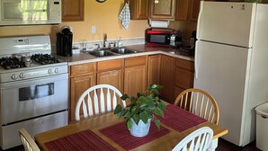 A kitchen with wooden cabinets, a stove, microwave, and a refrigerator. There is a dining table with chairs and a plant on it. - One Bedroom One Bath Apartment (Selmer)