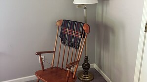 A wooden rocking chair with a plaid blanket, a framed certificate on the wall, and a floor lamp. - One Bedroom One Bath Apartment (Selmer)