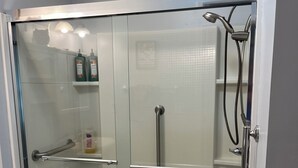 A glass-enclosed shower with a handheld showerhead, a handheld showerhead, and a handheld showerhead. - One Bedroom One Bath Apartment (Selmer)
