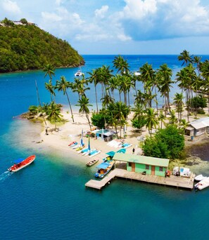A tropical beach with a dock, palm trees, and a small building.