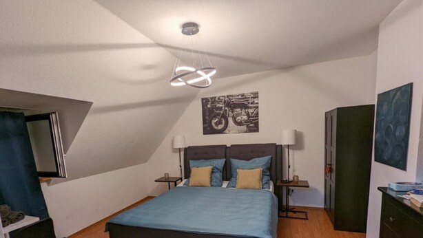 Un dormitorio con cama, dos mesitas de noche, un armario y una lámpara en el techo.