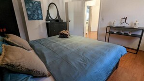 Un dormitorio con cama, cómoda, espejo y repisas con adornos.