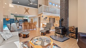 A spacious living area with a high ceiling, a fireplace, and a kitchen in the background.