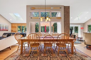 Uma sala de jantar com mesa e cadeiras de madeira, janelas amplas e vista para o exterior.