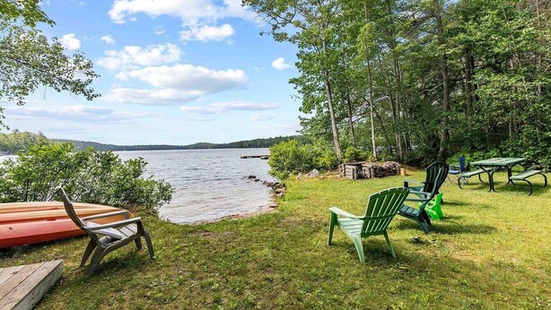 A lakeside park with picnic tables and chairs, a wooden deck, and a view of the lake.