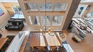A spacious living area with a wooden dining table, comfortable seating, and large windows providing natural light.