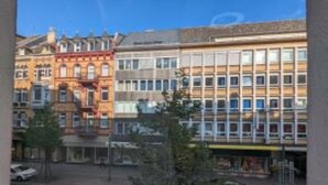 En byggnad med flera våningar som kombinerar olika arkitektoniska stilar, inklusive en röd byggnad med utsmyckade detaljer och en modern byggnad med ett rutmönster av fönster.