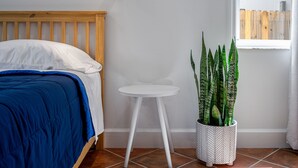 Een slaapkamer met een houten hoofdbord, een witte ronde bijzettafel en een potplant met groene bladeren.