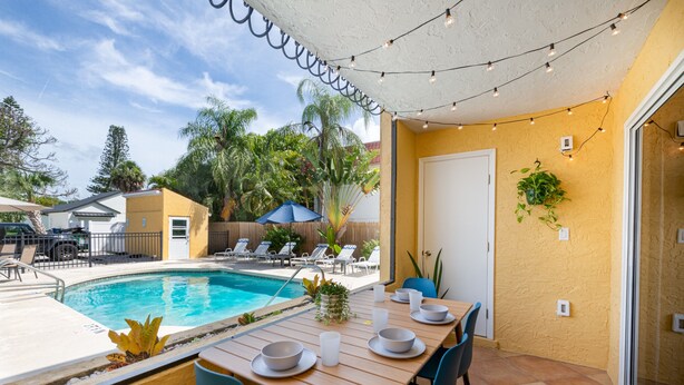 Een zwembadterras met een houten eettafel, lounge stoelen en een overdekte patio.