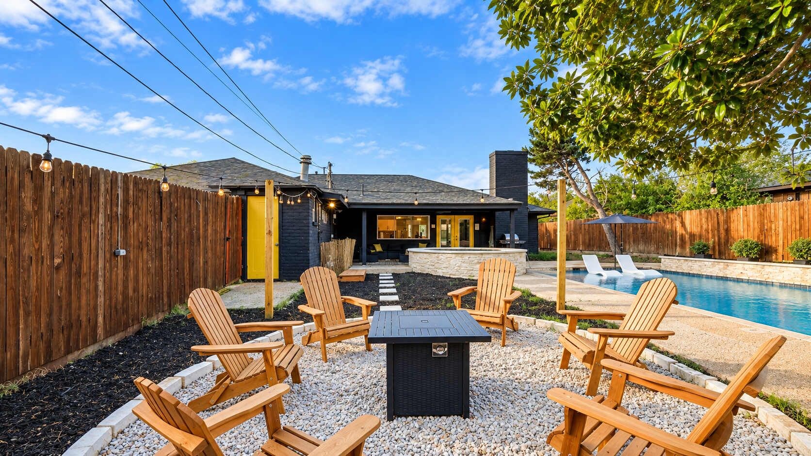 A backyard with a pool, wooden chairs, a fire pit, and a wooden fence.