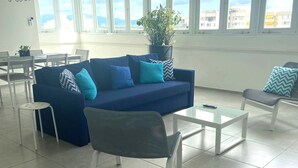 A modern living room with a blue sofa, white chairs, a glass coffee table, and a potted plant.