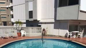 A swimming pool with tiled edges, surrounded by lounge chairs and a potted plant.
