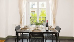 A dining table set for four with chairs, a bottle of wine, and a window with curtains.