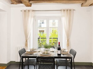 Una mesa de comedor preparada para cuatro personas, con sillas, una botella de vino y un ventanal con cortinas.
