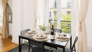 A dining area with a table set for two, a bottle of wine, and a view of a balcony with greenery.