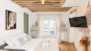 A bedroom with a bed, a TV mounted on the wall, a window with curtains, and a view of the outside. - Authentic parisian property in the Marais (Paris)