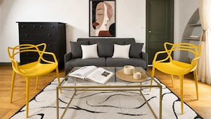 A living room with a sofa, two yellow chairs, a glass coffee table, a black cabinet, and a framed artwork on the wall. - Authentic parisian property in the Marais (Paris)