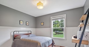 Ein Schlafzimmer mit Bett, Fenster und Schreibtisch mit Lampe.