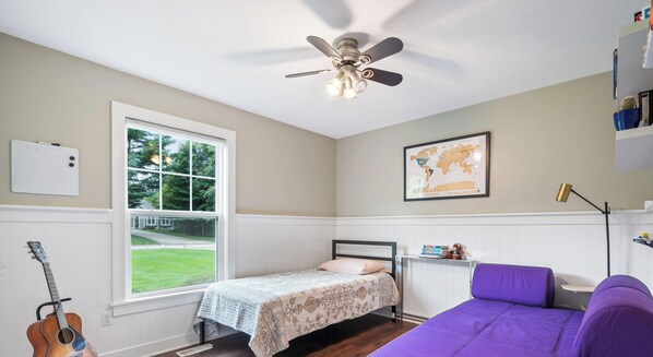 Un dormitorio con una cama, un ventilador de techo, una ventana, una guitarra, un mapa en la pared y una silla morada.