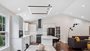 A modern kitchen with white cabinetry, a central island, and a dining area with a table and chairs. - Destined for Relaxation (Saugatuck)