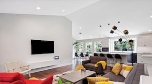 Ein modernes Wohnzimmer mit Flachbildfernseher, einer Couch, einem roten Sessel und einem Essbereich mit Bar.
