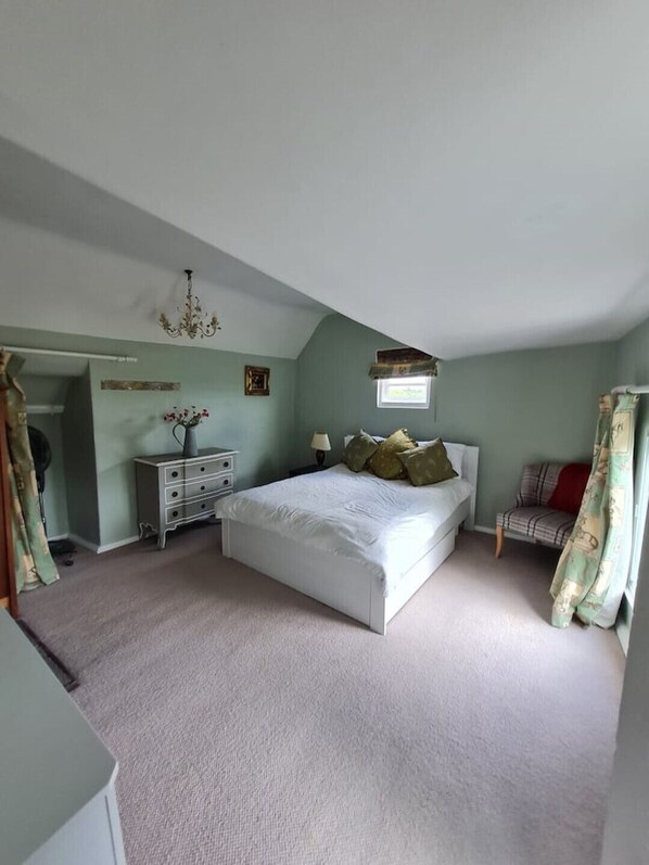 A bedroom with a large bed, a dresser, a nightstand, a chandelier, and a window.