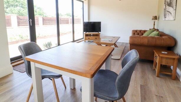 A modern living room with a wooden table, two chairs, a sofa, and a television. - Swallow Cottage (Sandbach)